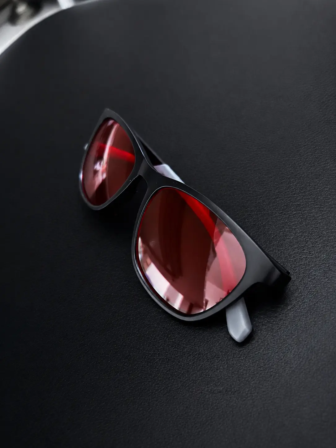 Lumiq blue light blocking glasses angled view, red lenses on dark surface
